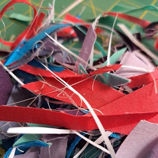 Red, purple, and blue scraps in a pile on a green cutting mat.