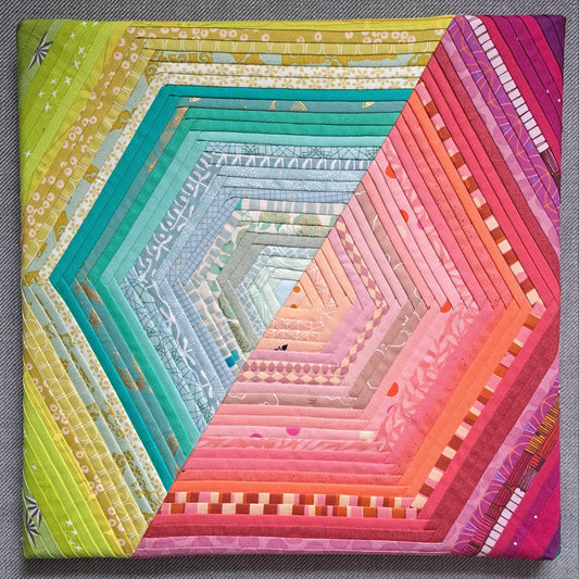 A hexagon made of two halves - one green and one pink - using quarter-inch foundation paper pieced sections. Mounted onto a canvas.